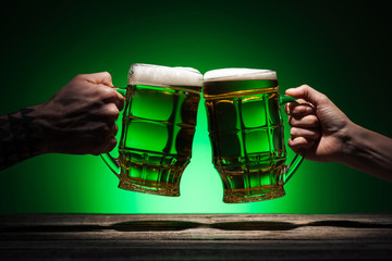 cropped view of friends toasting with glasses of beer on st patricks day on green background