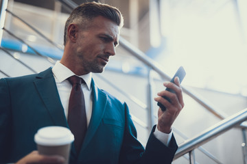 Man with beverage reading message on telephone