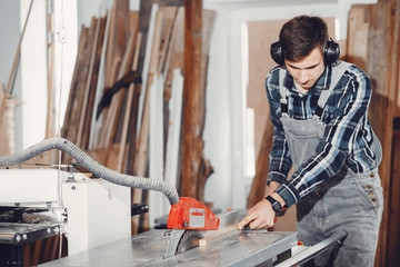 A man carves a tree. The carpenter works with saw in a studio. An engineer provides a tree shape