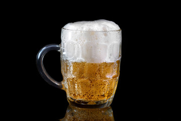 A glass of light beer on a black background with reflection
