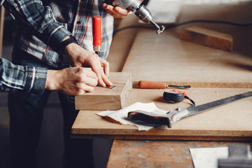 A man carves a tree. The carpenter works with a drill in a studio. An engineer provides a tree shape