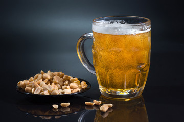 Mug of light beer and peanut on a dark background. Snack for alcohol