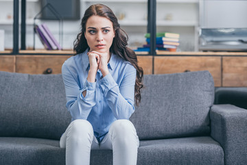 sad woman in blue blouse and white pants sitting on grey couch in kitchengrieving disorder concept ,