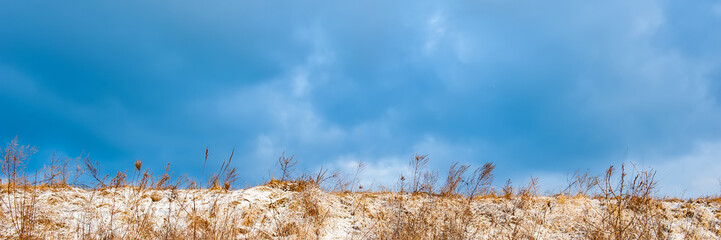 Obraz premium hill covered with snow and dry grass against the blue sky.