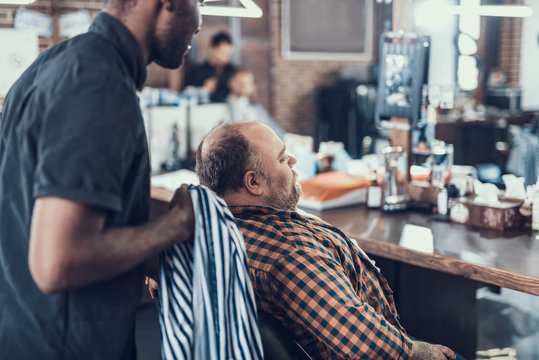 Attractive master preparing visitor to hair cutting
