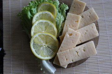 Cheese and lemon lie on a plate. The dish is decorated with a green leaf of lettuce