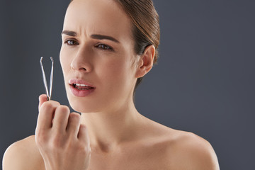 Obraz premium Lovely young woman looking at on tweezer in her hands