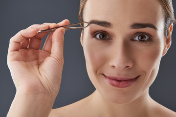 Pretty lady with tweezer in hands looking at camera