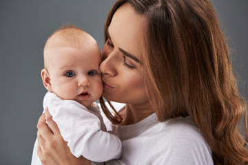Charming mama kissing her lovely baby in cheek