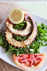 Grilled octopus on lettuce leaves with lemon and tomato slice