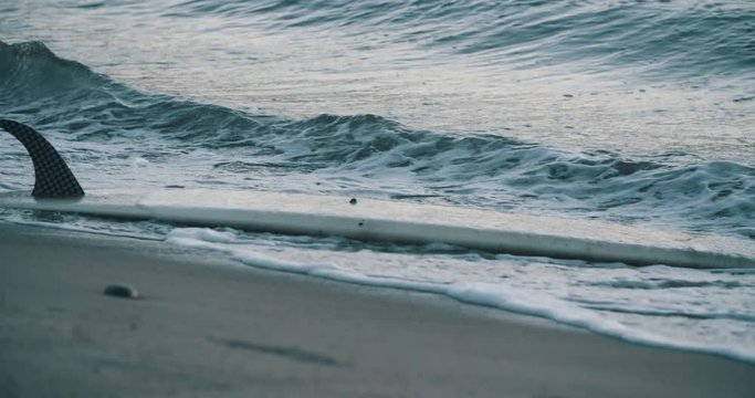 Loose surfboard washed up on beach bashing in waves