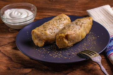 cabbage rolls stuffed with ground beef and rice served on a white plate on an old rustic table with sour cream in a bowl, view from above, close-up, flatlay