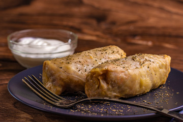 cabbage rolls stuffed with ground beef and rice served on a white plate on an old rustic table with sour cream in a bowl, view from above, close-up, flatlay