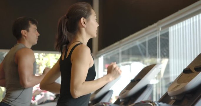Attractive asian girl running on the treadmill in the sport gym. Slow Motion.