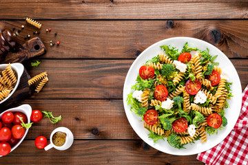 Italian pasta salad with wholegrain fusilli, fresh tomato, cheese, lettuce and broccoli on wooden...