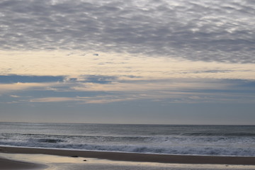 The waves in the calm sea meet the patterned cloud in the morning sky in Gisborne, New Zealand.