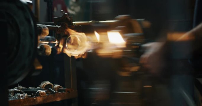 Slow motion close up of glass blower working with flame on a handmade wine glass from precious crystal in a workshop. Shot in 8K. Concept of handmade,high quality, artisan, made in Italy,glass blowing