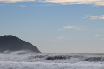 Waves crash on the shore as the cliffs stand above the beach in Gisborne, New Zealand.
