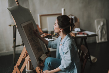 Beautiful lady drawing on the canvas while being alone in her studio