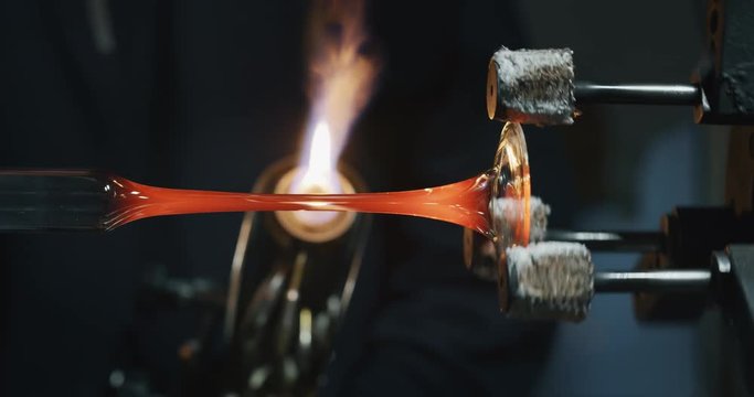 Slow motion of experienced glass blower working with flame on a handmade art piece of glass from precious crystal in a workshop.