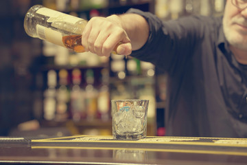 Bartender man pours whiskey to the client of the hotel bar. The concept of service. Toning