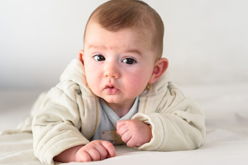 Beautiful and sweet newborn baby lying face down on the bed raising his head to look at the camera curiously.