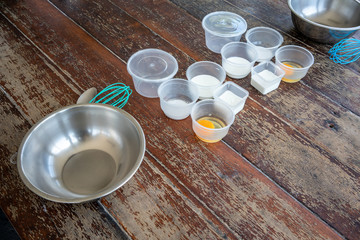 Prepared ingredients for making homemade ice cream with mixing bowl and whisker on wooden table.