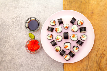 Romantic heart sushi dinner. Maki rolls with ginger, wasabi and soy sauce on rosy plate. Concept for Valentine's Day or March 8th. Stone and wooden background, top view