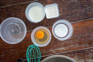 Prepared ingredients for making homemade ice cream with mixing bowl and whisker on wooden table.