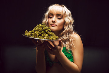 Blonde caucasian woman in cannabis bikini poses with tray of marijuana buds - 249624129