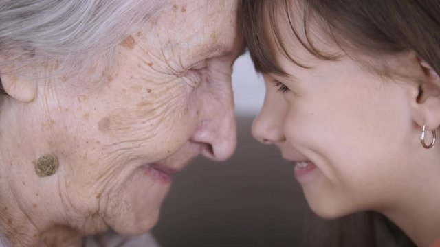 Portrait of a grandmother with granddaughter. Happy old granny and young girl look into each other's eyes with their foreheads buried.