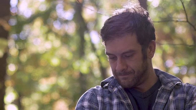 Sad, frustrated handsome man thinking and looking down in the woods