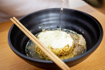 Dipping boiling water into instant cheese noodle close up.