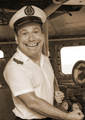 A laughing sailor officer in the uniform is steering the ship with a rudder. The funny captain...