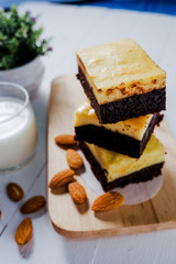 A stack of chocolate cheese cake brownies on wooden background with almonds seed and milk.close up