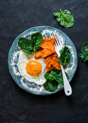 Healthy breakfast or snack - fried egg, baked sweet potato and spinach on dark background, top view. Copy space