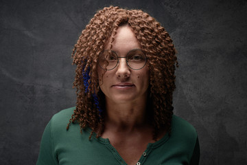 Portrait of an authentic adult woman with afro curls against a black wall in the studio. Unusual...