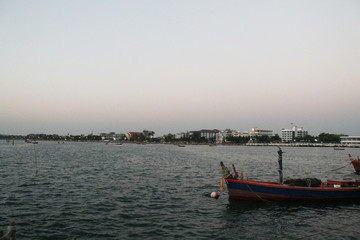 Naklejka premium fishing boat in the sea and sunset sky and city background