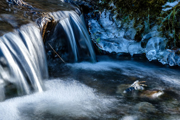 thin layer of ice on the rocks over the creek with water running down under the sun on a cold...