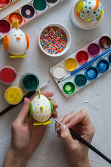Preparation for Easter. Multi-colored paint, hands in the frame paint the eggs. handmade chickens and Bunny from the egg