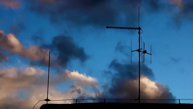 An antenna silhouette on an evening sky with fast-moving clouds. Sunset over the roof with an antenna.