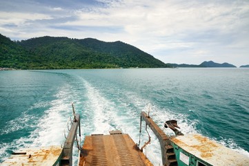 Ferry ramp and trace on the water of tropical sea behind ferry, with tropical Koh Chang island on...