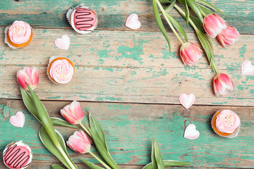 Frame of tasty cupcakes with tulips on vintage wooden table. Romantic love background. Copy space, overhead shot.