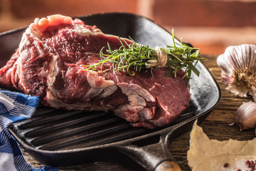 Raw beef steak in grill pan with salt pepper garlic and herbs on wooden table