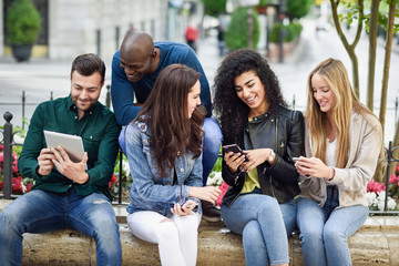 Multi-ethnic young people using smartphone and tablet computers outdoors