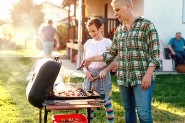 Mother and daughter grilling vegetables and meat on the sticks in backyard.