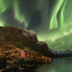 Famous tourist attraction Reine fishing village on Lofoten Islands, Norway with red rorbu houses in winter. Green Aurora borealis. Starry sky with polar lights. Night winter landscape with aurora. 