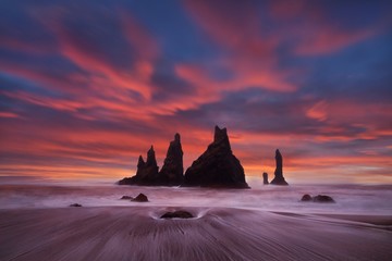 Reynisdrangar are volcanic basalt sea stacks situated under the cliffs of mountain Reynisfjall near the village Vik i Myrdal , southern Iceland which is framed by a black sand beach, Iceland.