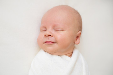 Newborn baby boy on a white background. Baby smiles. Boy is sleeping. White baby wrap