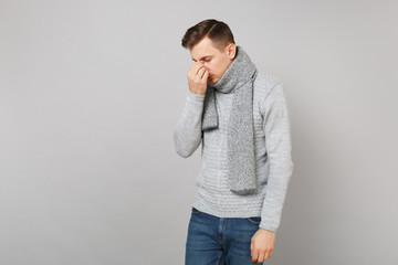 Disappointed young man in sweater, scarf with lowered head holding hand on nose, face isolated on grey background. Healthy lifestyle ill sick disease treatment cold season concept. Mock up copy space.